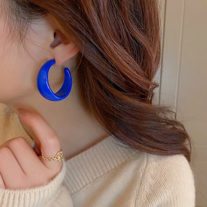 Detail of a shiny blue C-shaped hoop earring worn by a model in a lifestyle setting