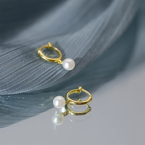 Close-up of golden pearl hoop earrings with mirror reflection on blue fabric
