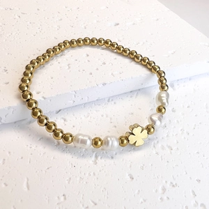 Detail of gold beads, baroque pearls and a clover charm on an elastic bracelet