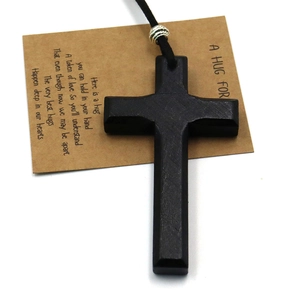 Nahaufnahme des schwarzen Holzkreuz-Anhängers mit Silberperle auf einer Grußkarte