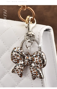 Detail of leopard print bow keychain with golden ring on white quilted luxury handbag