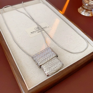 Detailed view of silver snake chain necklace with rectangular woven pendant on a tray