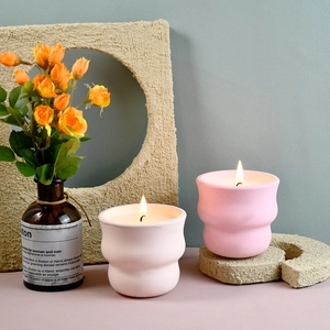 Dettaglio di portacandele ondulati in gesso rosa e crema con candele profumate accese