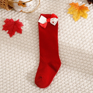 Detail of red Christmas socks with bows and reindeer charms on warm knit background