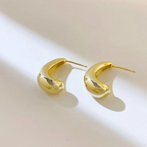 Macro detail of 18k gold plated C-shaped geometric earrings with polished finish and soft shadows