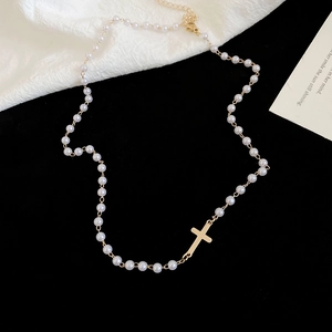 Detailed macro view of white pearl strand necklace featuring a polished gold cross pendant