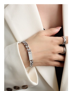 Close-up of polished silver chain bracelet and rope rings styled with a white blazer