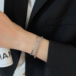 Close-up of three-piece silver snake and Cuban link chain bracelets on model wrist