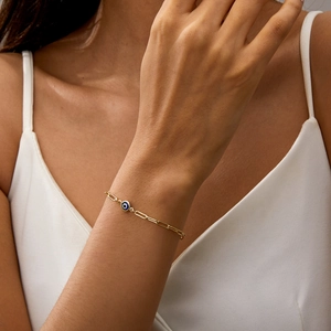 Detail of gold paperclip chain bracelet with blue evil eye pendant on wrist