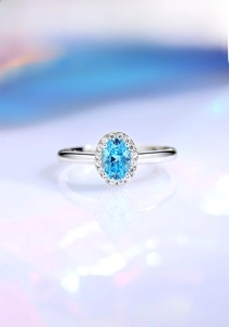 Macro shot of an oval-cut sky blue gemstone ring with sparkling diamond halo setting