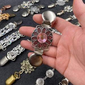 Detail of silver metal cardigan clip featuring a red flower and pink round gemstone