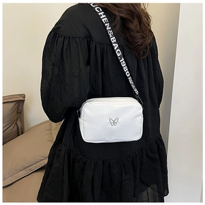 Close-up of white nylon crossbody bag with silver butterfly icon and lettered wide strap