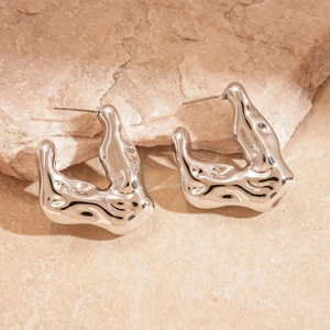 Detailed view of silver liquid metal texture C-shaped earrings on stone background