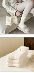 Detail of white plush socks with pink bow embroidery and cozy thermal wool texture