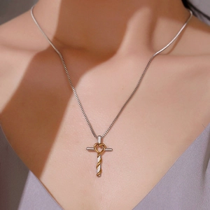 Cross and heart pendant necklace in gold and silver tones worn on a model's neckline