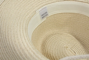 Detail view of woven paper straw hat showing the 100% paper material care label