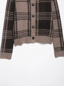 Macro shot of plaid knit cardigan with round neck and black buttons on earth tone fabric