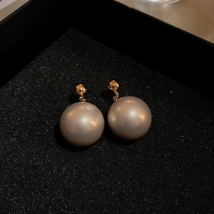 Detailed close-up of champagne-colored round pearl stud earrings with gold plating