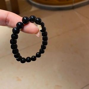 Macro shot of black obsidian beaded bracelet with a yellow pendant hanging from a finger