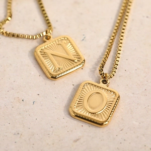 Detail of square gold pendants with initial letters N and O on a textured stone base