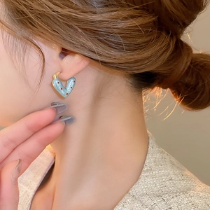 Detailed close-up of blue heart earring with red polka dots worn by a female model