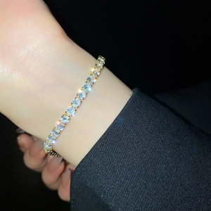 Macro shot of gold-plated tennis bracelet with white zircon stones on a black background