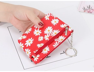 Close-up of red fabric coin purse featuring white daisy patterns and metal zipper detail