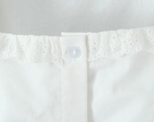 Detail of white blouse neckline featuring delicate hollow embroidery and resin button