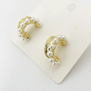 Detail showing elegant gold C-shaped earrings with white pearls on a display card