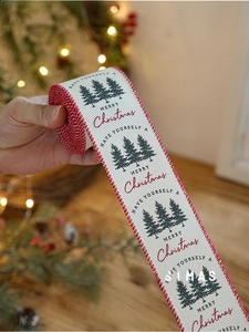 Detail of beige linen Christmas ribbon with red edges and green pine tree prints