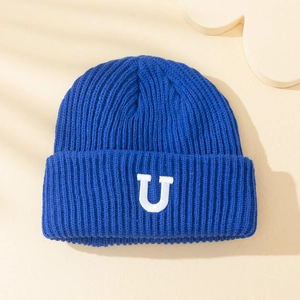 Bonnet en tricot bleu avec lettre U brodée blanche sur un fond beige minimaliste