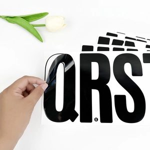 Peeling a glossy black 6-inch vinyl letter sticker from backing on white background