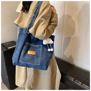 Close-up of a blue denim tote bag with brown leather patch and white cloud charm