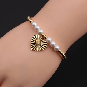Détail du bracelet perlé avec breloque cœur dorée au motif radial et petit cristal brillant