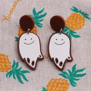 Close-up of white acrylic ghost earrings with smiling face on pineapple fabric background