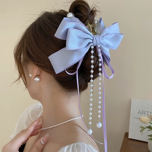 Detail view of purple silk bow hair claw clip with elegant long pearl tassel strands