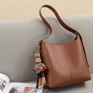Brown faux leather bucket bag for women with a cute rabbit charm on a modern sofa