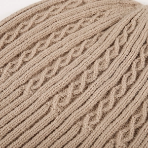 Close-up of beige cable-knit winter beanie showing thick warm wool texture and patterns