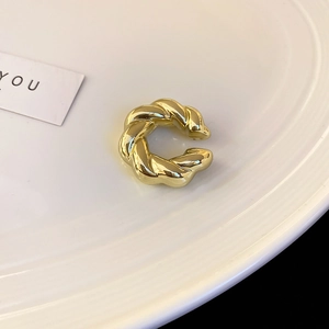 Gros plan d'un ear cuff doré torsadé style croissant sur une assiette en céramique blanche