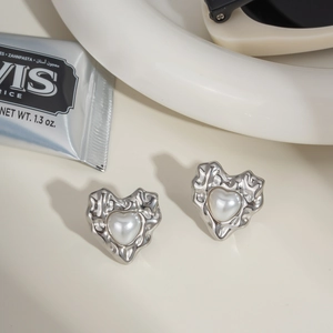 Detail of silver heart earrings with lava texture and white pearl inlay on beige background