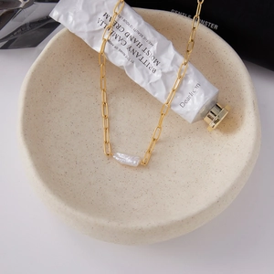 Detail van gouden paperclip ketting met een barokke zoetwaterparel in een schaal