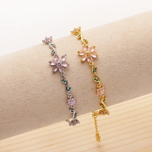 Macro detail of cherry blossom bracelet with pink and green zircon stones on jewelry scroll
