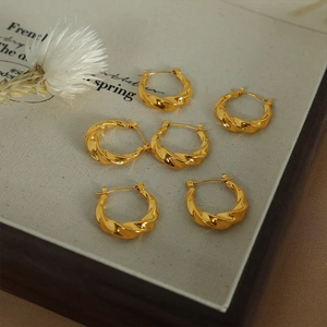Créoles torsadées minimalistes plaquées or 18 carats sur un plateau en lin gris