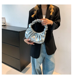 Detail of silver pleated cloud bag with metallic finish held by model in casual suit