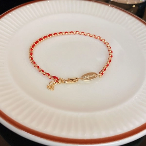 Detailed macro of a woven red string bracelet featuring gold beads and a metal clasp