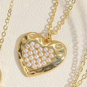 Macro detail of golden heart pendant featuring hammered texture and white pearls