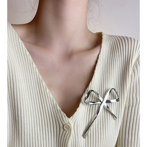 Detail view of a silver metallic bow brooch worn on a beige knit sweater for women