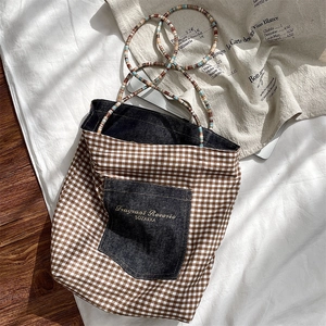 Detail of vintage checkered canvas tote bag with denim pocket and colorful beaded handle