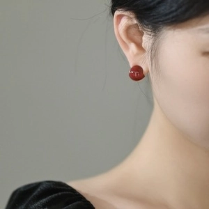 Close-up of a model wearing minimalist red round stud earrings with a glossy finish