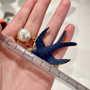 Close-up of vintage blue enamel swallow brooch with white pearl measuring 5cm on a ruler